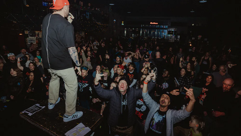 Vocalist on the stage edge facing a packed crowd at Louisville Loves Nu-Metal